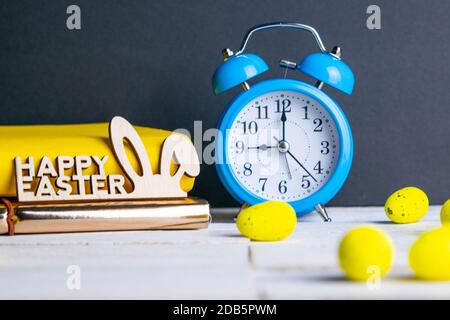 Easter concept, clock and apple, yellow books, eggs are scattered next to them, there is a wreath in the background. Stock Photo