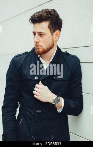 A Caucasian male wearing a white shirt and a black coat posing against a white wall Stock Photo
