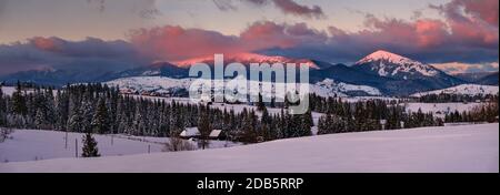 Alpine village outskirts panorama in last evening sunset sun light. Winter snowy hills and fir trees, magnificient and picturesque mountain range in f Stock Photo