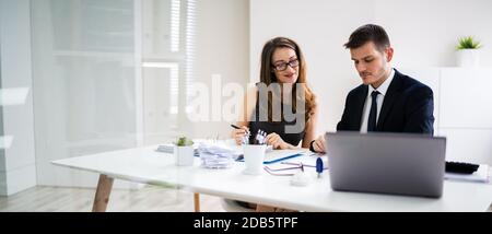 Two Young Businesspeople Calculating Invoice With Calculator Stock Photo