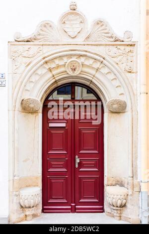 Historic entrance portal from 1736 with a coat of arms. Richly decorated archway with a brown wooden door of a listed house Stock Photo