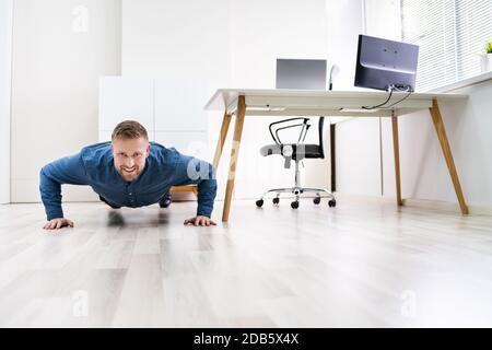 Businessman Doing Push Up On Hardwood Floor In Office Stock Photo