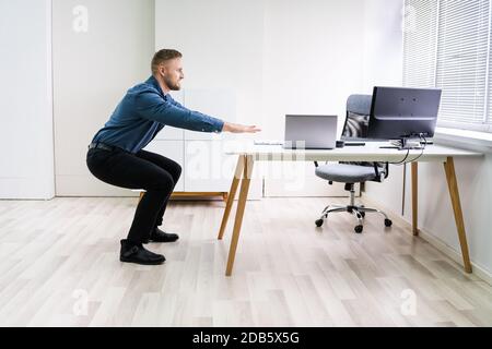 Smiling Young Businessman Doing Sit-ups At Workplace Stock Photo