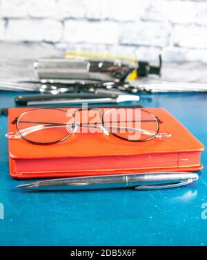 Hairdressing tools set, Red notepad with glasses and scissors, hair clipper, comb, dangerous razor, hair gel stand on blue background. Stock Photo
