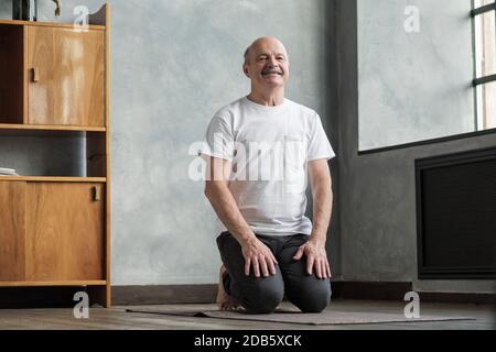 Senior man practicing yoga at home sitting in Vajrasana pose. Stock Photo