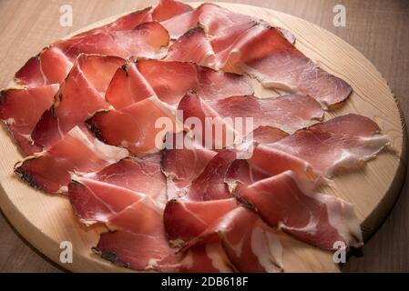 Speck, typical smoked ham from South Tyrol, Alto Adige in Italy - slices on wooden cutting board in top view Stock Photo