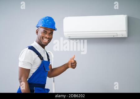 Smiling Male Electrician Gesturing Thumbs Up Near Air Conditioner Stock Photo
