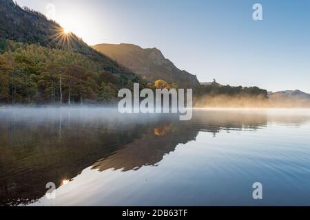 Calm and peaceful misty Autumnal morning at Derwentwater in the Lake District as the sun rises above the mountains. Stock Photo