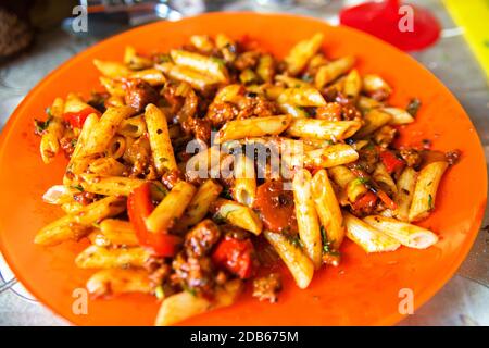 Italian pasta bolognese served on orange plate. Heaped plate of delicious Italian macaroni with tomato, fresh basil leaves and grated parmesan cheese Stock Photo