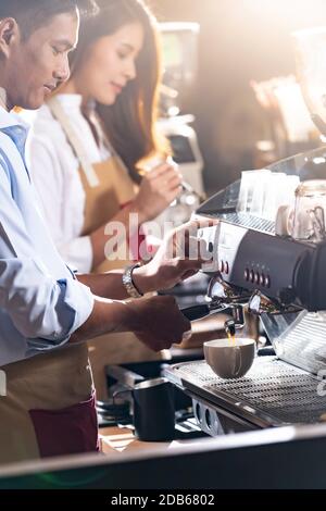 Side view shot of a barista brewing coffee by modern coffeemaker machine to making a cup of coffee with other barista working in background. Using for Stock Photo