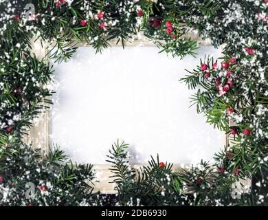 Christmas tree branches with red berries and frame paper card note and flying snowflakes. Copy space for text. Nature New Year concept. Flat lay. Stock Photo