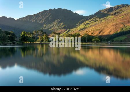 Beautiful morning sunlight shining on Buttermere in the Lake District with mirror like reflections. Stock Photo