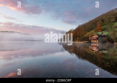 Boathouse at Ullswater Lake with beautiful dawn sunrise colour in the sky, lake mist and calm reflections. Stock Photo