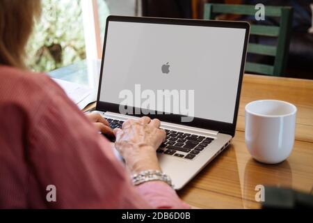 ROSARIO, ARGENTINA - NOVEMBER 16, 2020: Apple logo in the screen of laptop. Mature woman sitting in front of computer with mac os x operating system Stock Photo