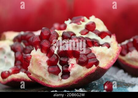 Broken pomegranate with bright red grains close-up on a background of whole pomegranate fruits on a wooden surface with snow outdoors in winter. Stock Photo