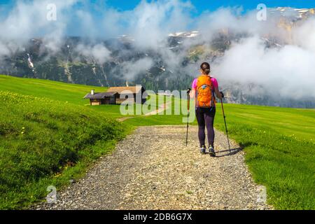 Hiking trail with wooden huts. Sporty backpacker hiker woman walking on the path in the mountains, Alpe di Siusi, Dolomites, Italy, Europe