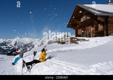 Two happy alpine skier and snowboarder throwing cheerful snow in air in front of Swiss chalet and blue sky. Hasliberg Switzerland. Stock Photo