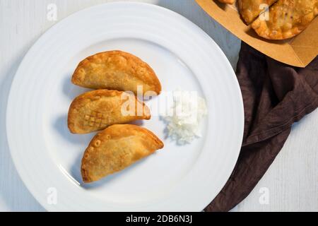 Traditional baked Argentinian empanadas savoury pastries with meat beef stuffing with fresh onion on white plate from above. Stock Photo