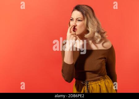 This is lie! Portrait of angry woman with blonde hair touching nose, showing liar gesture, expressing distrust of false suggestion, deception. Indoor Stock Photo