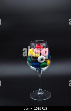 Wine glass filled with wooden circles of many colors on black background Stock Photo