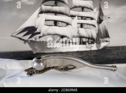 A Boatswain's whistle, or pipe, with a square-rigged sailing ship in the background. Stock Photo