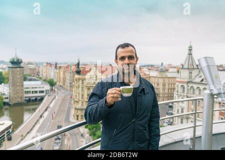 A male of mixed race stands on a balcony drinking coffee or tea Stock Photo