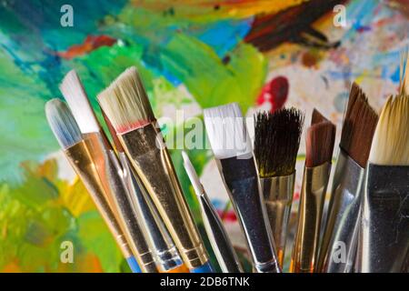 A group of different sized artist paintbrushes in a brightly colored holder in front of the painter's palette. Stock Photo