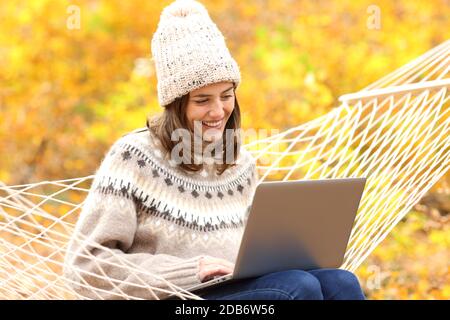 Happy woman using laptop sitting on hammock in fall season in a forest Stock Photo