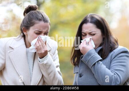 Two women blowing on tissue with flu symptoms standing in a park in winter Stock Photo