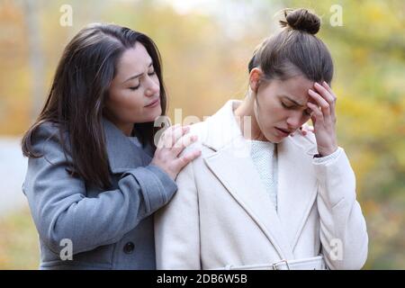 Woman comforting her sad best friend who is complaining in a park in winter Stock Photo