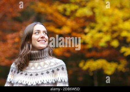 Happy woman looks at side contemplating standing in a park in autumn Stock Photo