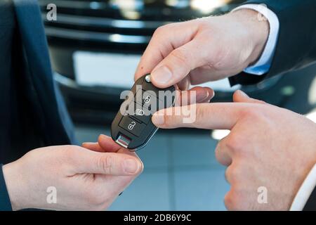 Car salesman hands over car keys to customer in the dealership and explains functions Stock Photo
