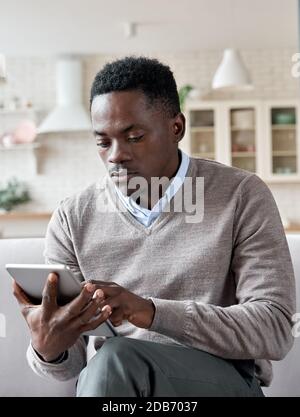 Serious african man using digital tablet apps sitting on couch at home. Stock Photo
