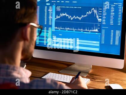 Stock market trader looking at computer trading online monitoring graph. Stock Photo