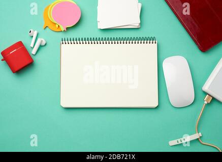 open notebook with blank white sheets, computer mouse, wireless headphones and charger, top view Stock Photo