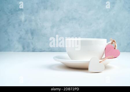 Two hearts are tied to the handle of a coffee Cup on a blue and white background. Stock Photo