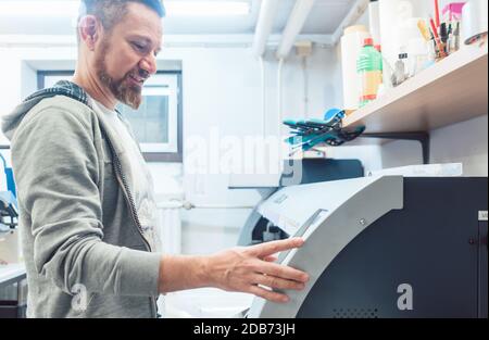 Man working on large format printer in advertising material agency operating the machine Stock Photo