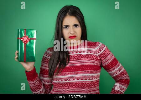 Young beautiful girl holding gift over isolated white background skeptic and nervous, disapproving expression on face with crossed arms Stock Photo