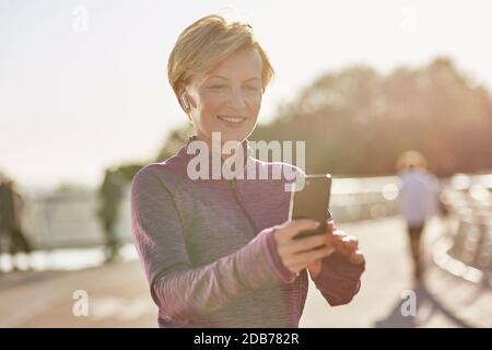 Results speak for themselves. Portrait of joyful active mature woman in sportswear using her smartphone, checking result after running outdoors on a Stock Photo