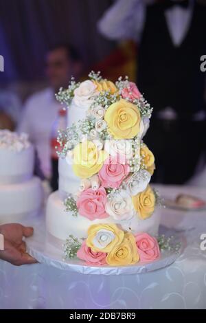 White wedding cake with white decorations and colorful roses on three floors. Wedding concept. Stock Photo