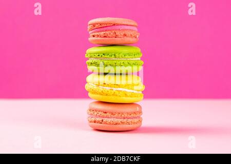 Multi-colored macaroons stand in a pile on a pink table. Close-up Stock Photo