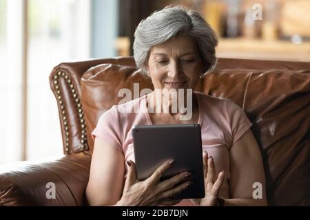 Close up smiling mature woman using tablet, having fun online Stock Photo