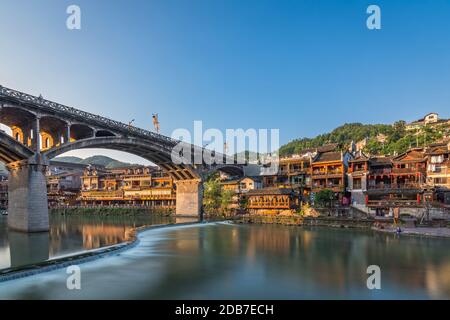 Feng Huang, China -  August 2019 : Long time exposure of the road bridge over Tuo Jiang river and wooden houses in ancient old town of Fenghuang known Stock Photo