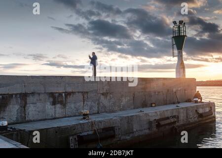 Middle aged  man wearing face mask, taking selfie photos on the harbour pier during sunset,Burgas Harbour, Bulgaria Stock Photo