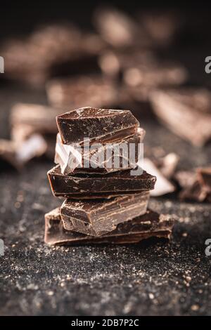 Pieces of chocolate bar. Broken dark chocolate on black table. Stock Photo