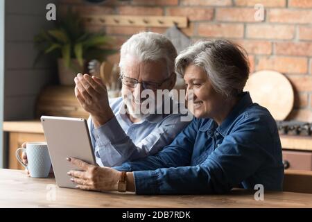 Happy mature couple having fun with tablet, sitting in kitchen Stock Photo