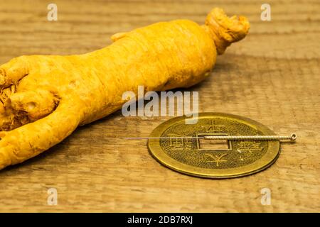 Acupuncture needle on Chinese coin with ginseng root Stock Photo