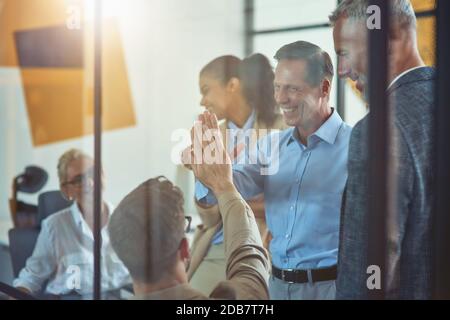 Two excited coworkers giving high five to each other and smiling while having a meeting with colleagues in the modern office Stock Photo