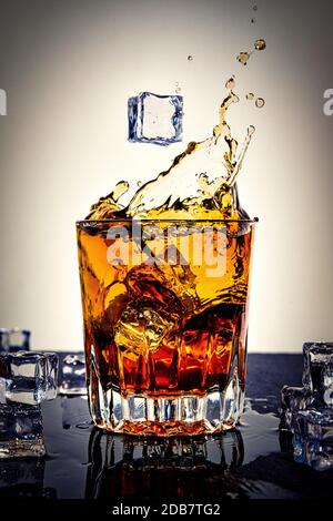 Photo of a drink on ice in a glass, with a falling ice cube. Stock Photo