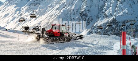 Red modern snowcat ratrack with snowplow snow grooming machine preparing ski slope piste hillalpine skiing winter resort Ischgl in Austria. Heavy Stock Photo